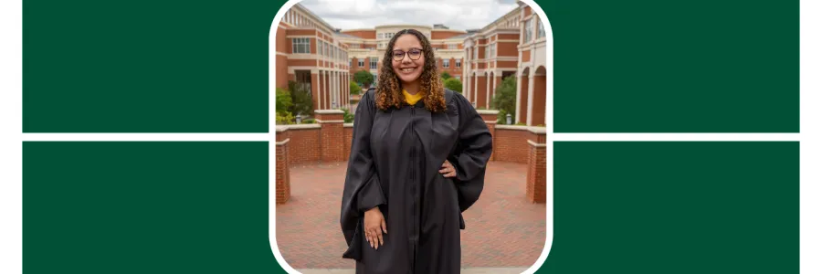 Carmen Rudd poses with her left hand on her hip and the right hand to her side, she wears a black grad gown. Her hair is curly and light brown. She smiles in front of the student union at unc charlotte 