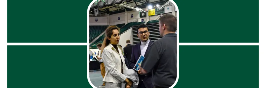 Two students wearing two piece suits, one with long hair and one with short, speak with a recruiter at a career fair.