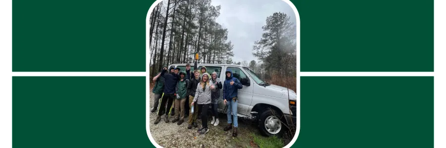 Students at the Audubon Center in S.C. pose in front of a UNC Charlotte van, it is rainy and they wear jackets.