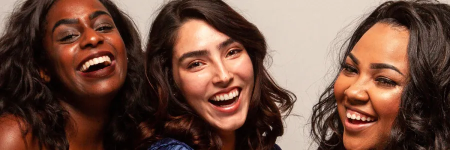 3 Women with different skin tones (Left: Dark, Center: White, Right: Medium) laughing joyfully on beige background