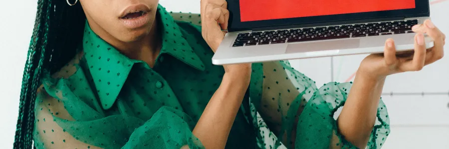 Woman holding laptop with word Scam on Bright red background