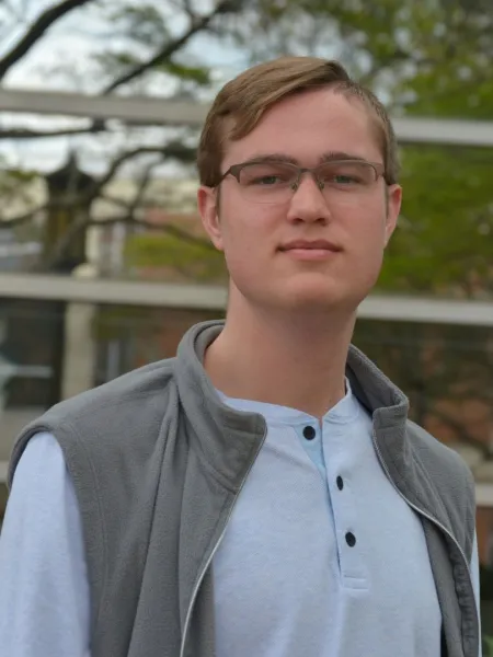 Carl poses in front of a glass building and some trees