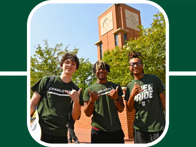 Photo of 3 niners wearing green, smiling down at the camera, holding up the pick axe hand gesture