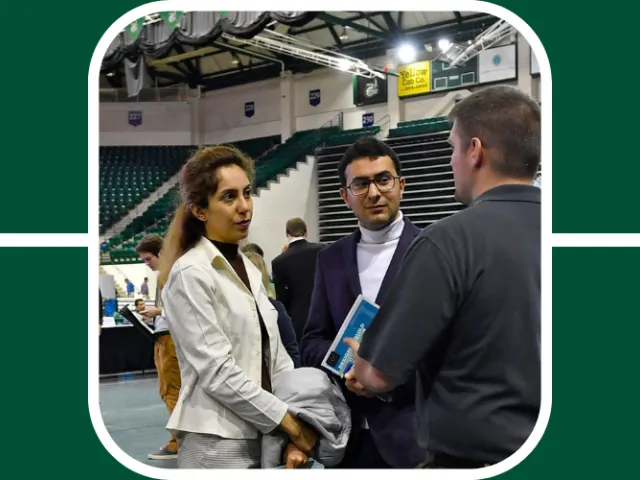 Two students wearing two piece suits, one with long hair and one with short, speak with a recruiter at a career fair.