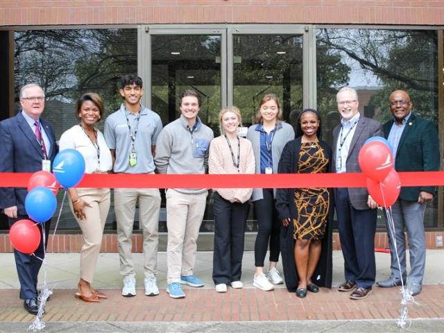 A group of employees at Piedmont Airlines poses behind red tape and red and blue balloons