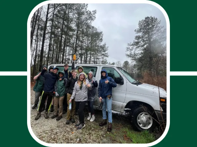 Students at the Audubon Center in S.C. pose in front of a UNC Charlotte van, it is rainy and they wear jackets.